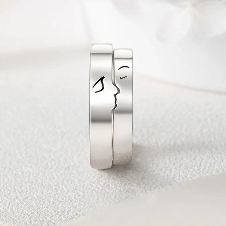 A close-up of two matching silver rings, designed to fit together to form a subtle kissing silhouette