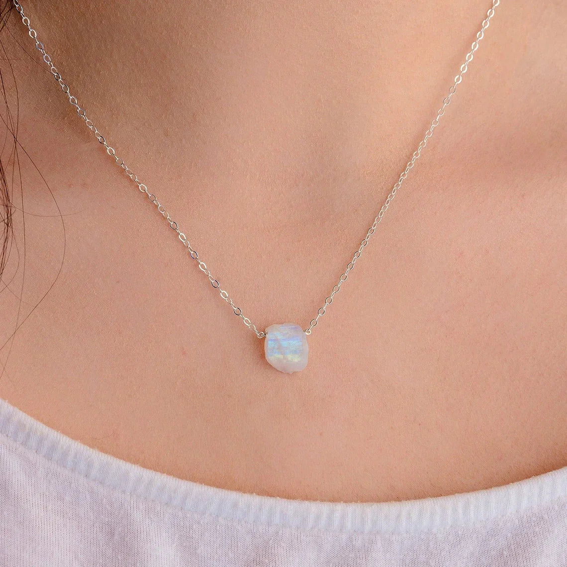 Close-up of a teardrop-shaped Rainbow Moonstone pendant on a delicate silver chain, showcasing the stone's iridescent blue hues