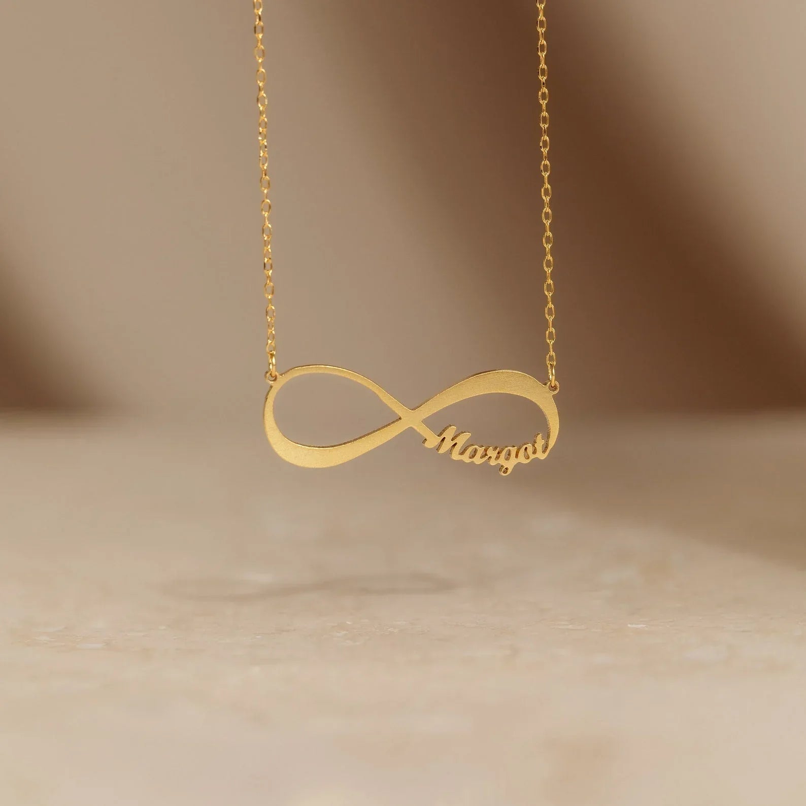 Detailed view of the gold Personalized Infinity Necklace, featuring elegant engraved words on a modern infinity pendant