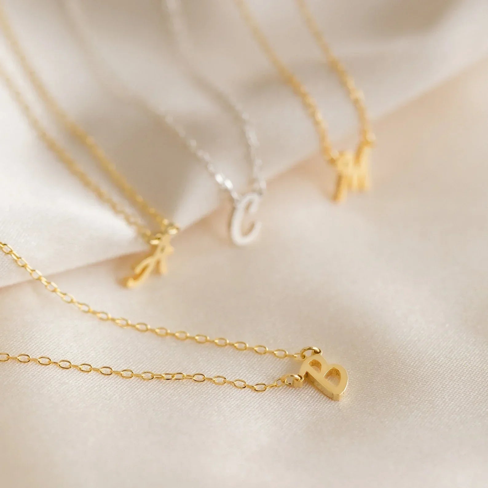A collection of Eraya Jewel Initial Letter Pendants featuring the letters 'A,' 'B,' 'C,' and 'M,' demonstrating the variety of options available for personalization.