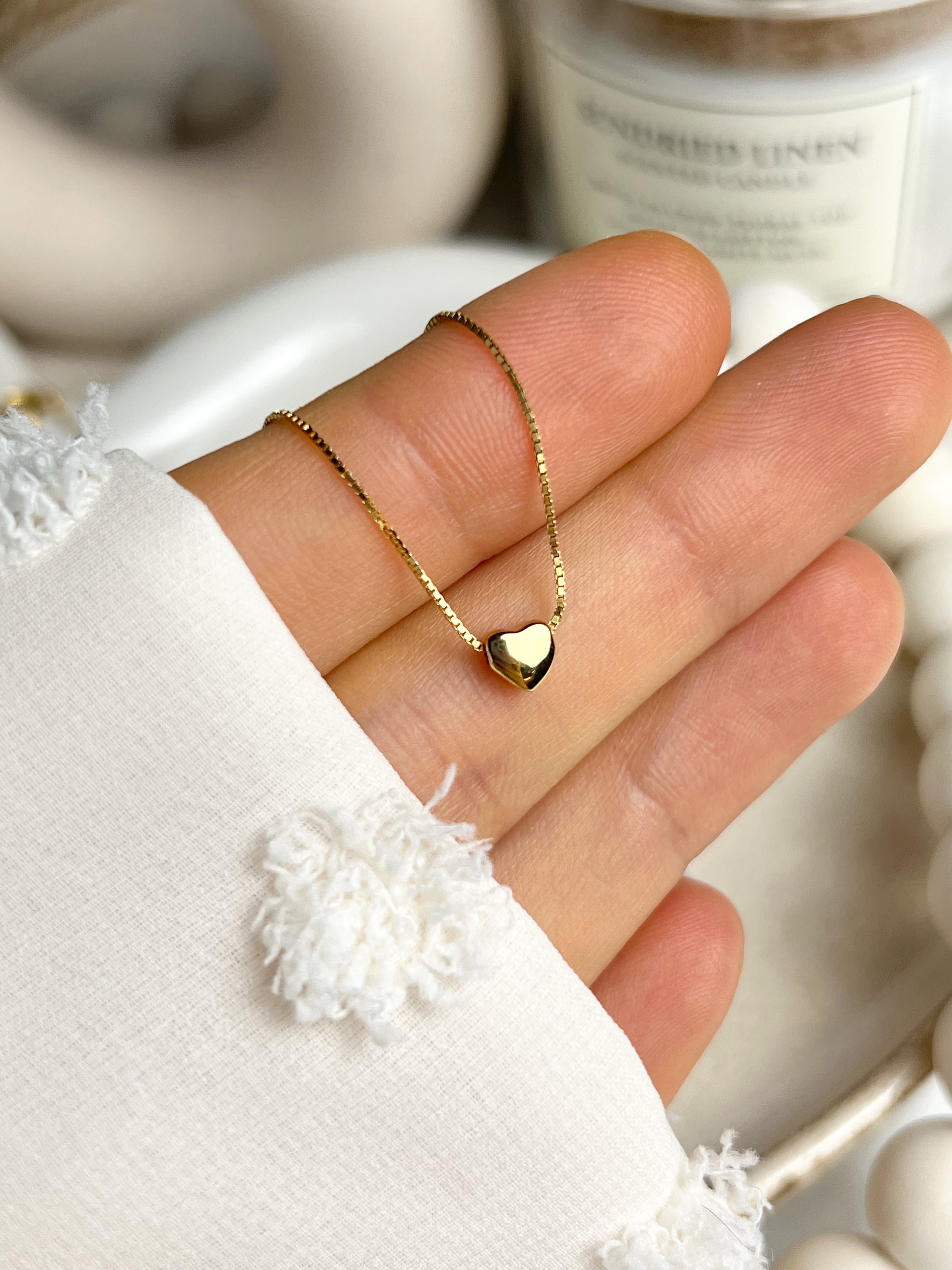 Model holding a tiny gold heart necklace delicately in her hand, showcasing its elegant shine.