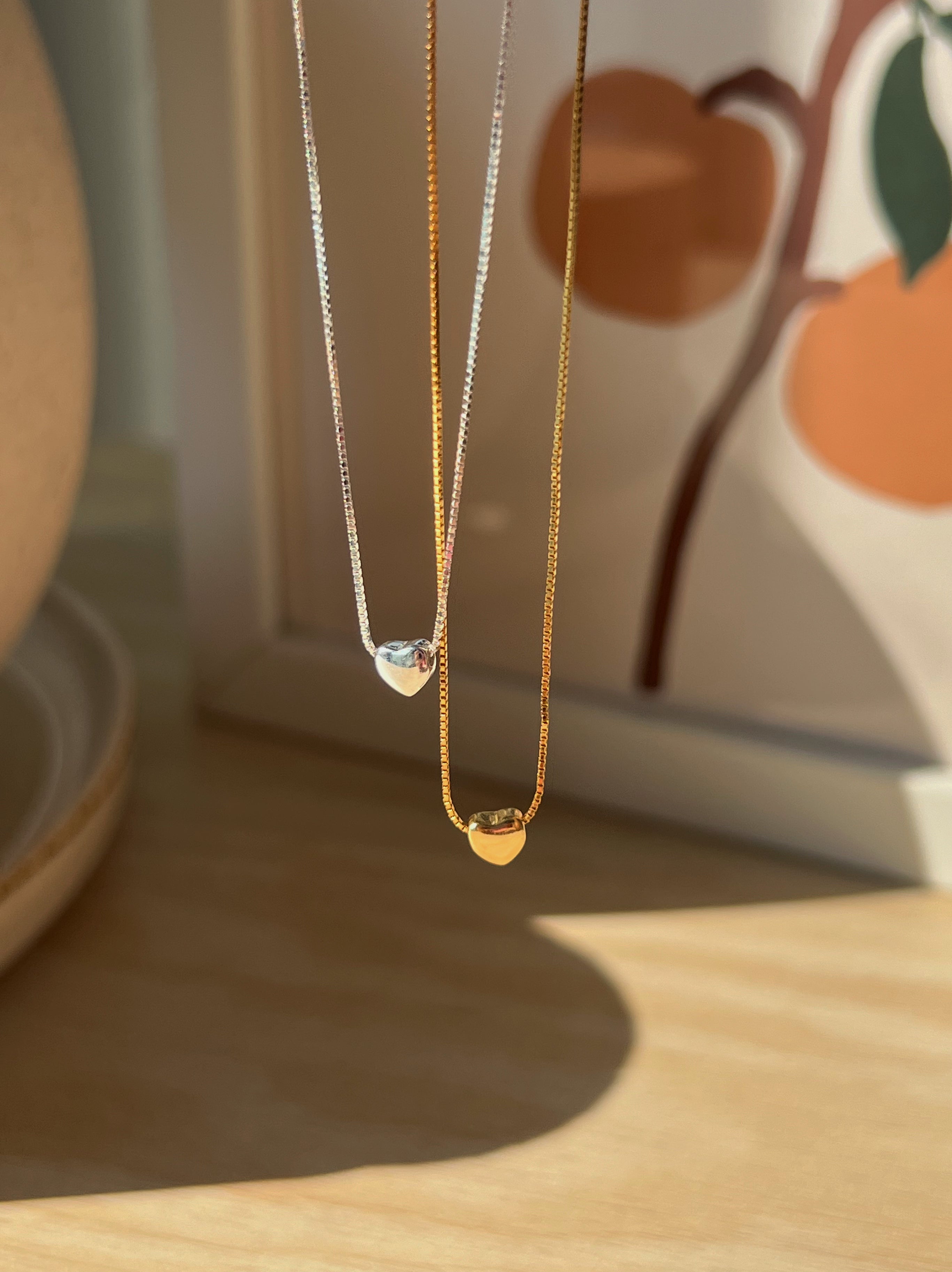 Side-by-side display of gold and silver heart necklaces, showing color options in the same elegant design.