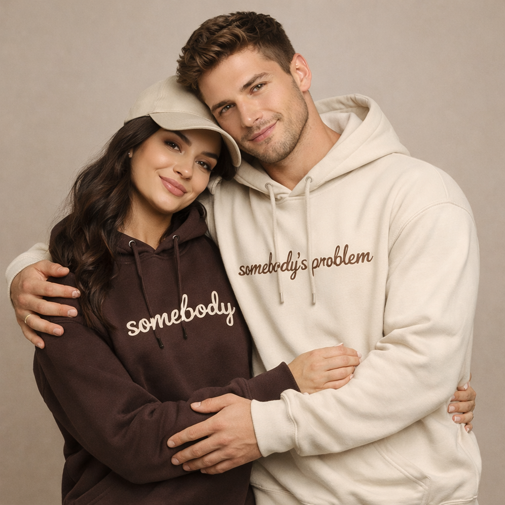 Couple hugging while wearing matching embroidered hoodies – dark brown hoodie with beige “somebody” embroidery and beige hoodie with brown “somebody’s problem” embroidery, premium couple hoodie set by Balaji Customi